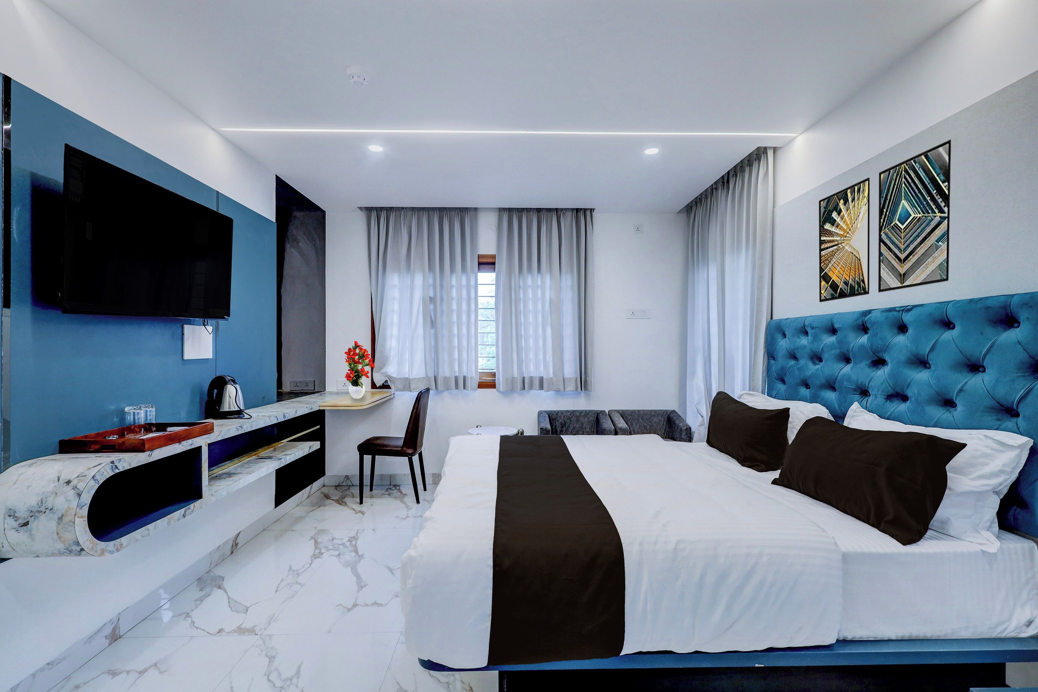 A modern hotel room with a large bed, a flat-screen TV, a desk, and a window with curtains.