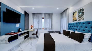 A modern hotel room with a large bed, a flat-screen TV, a desk, and a window with curtains.
