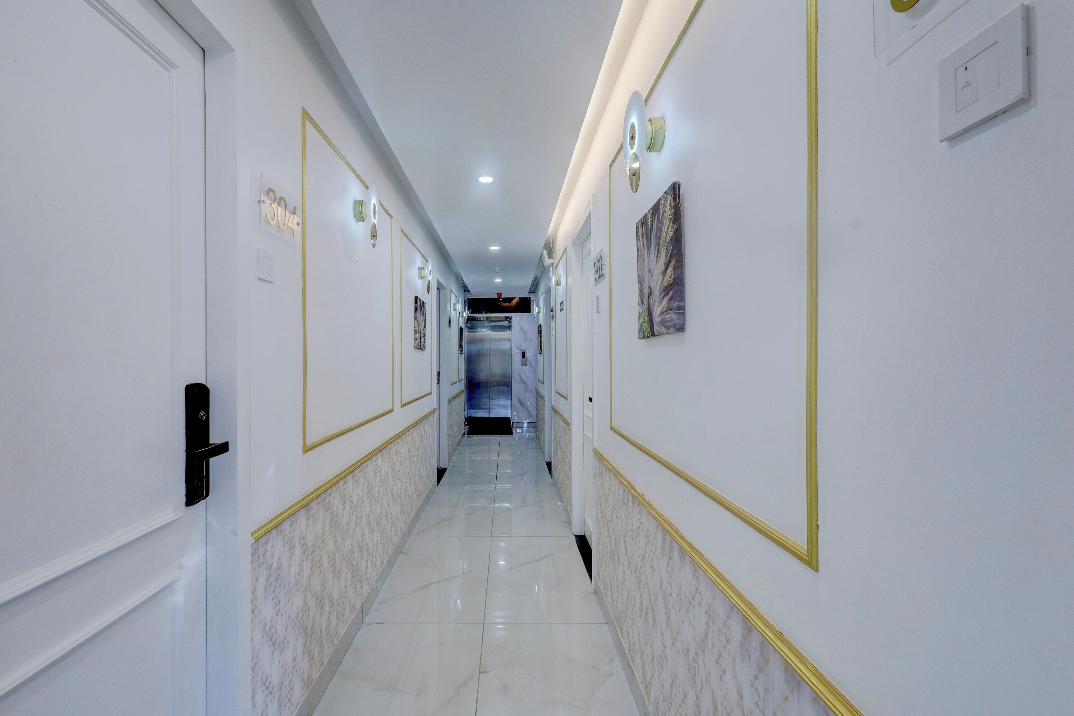 Un pasillo de hotel con puertas numeradas 304 y 302, piso de mármol y luces empotradas en la pared.