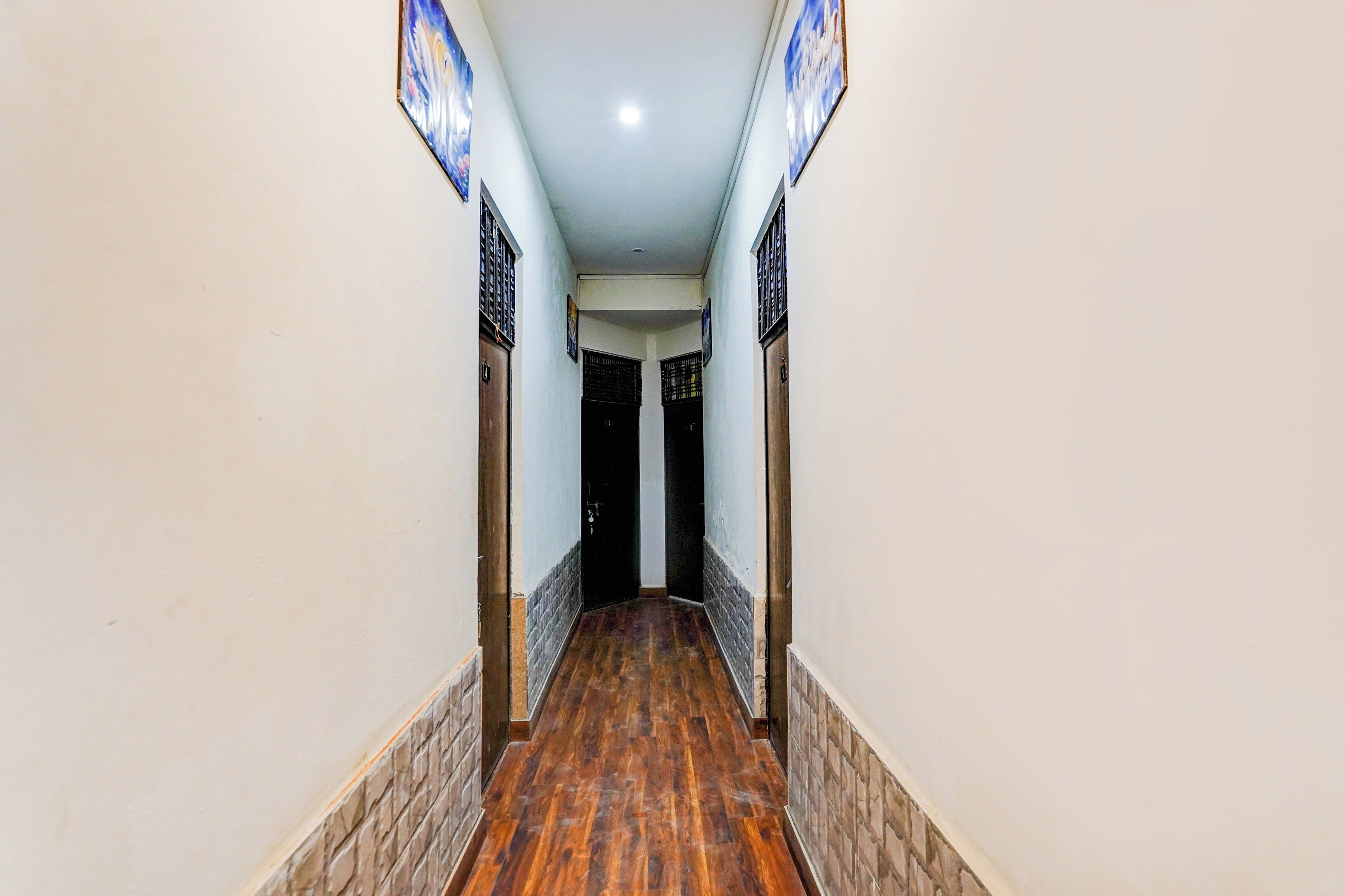 A hallway with wooden flooring, white walls, and doors with metal bars.