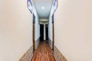 A hallway with wooden flooring, white walls, and doors with metal bars. - Hotel O George Town (Prayagraj)