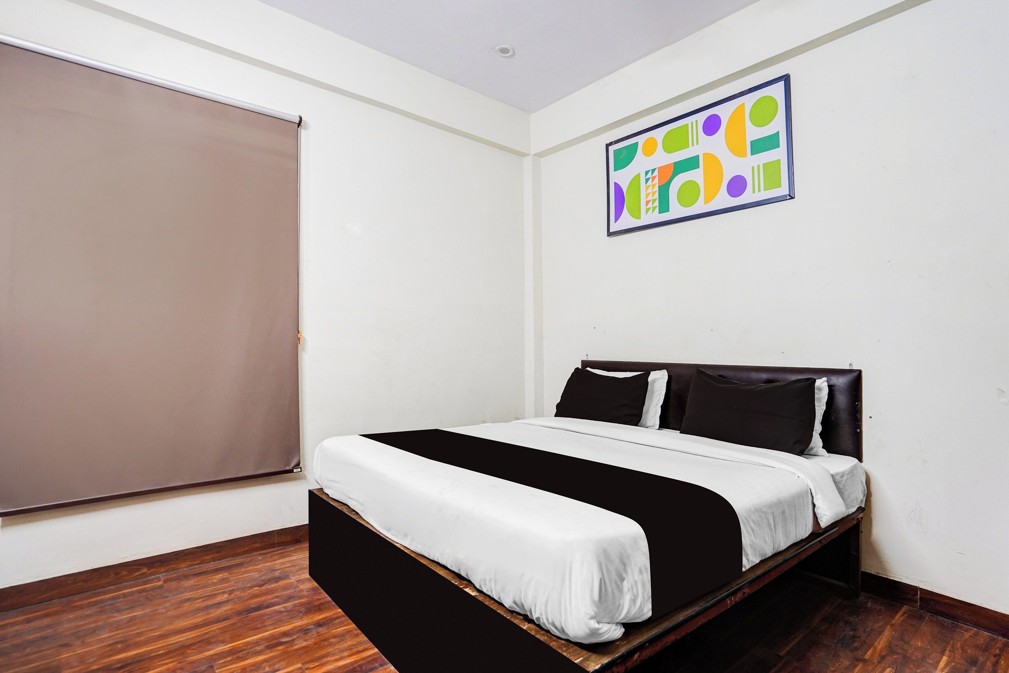 A bedroom with a bed, a window with a blind, and a colorful abstract painting on the wall.