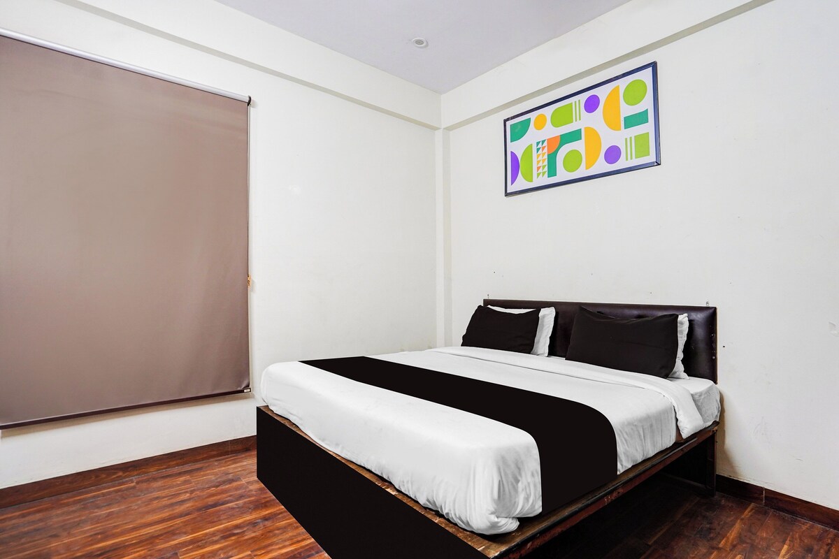 Un dormitorio con cama, ventana con persiana y un cuadro abstracto colorido en la pared.