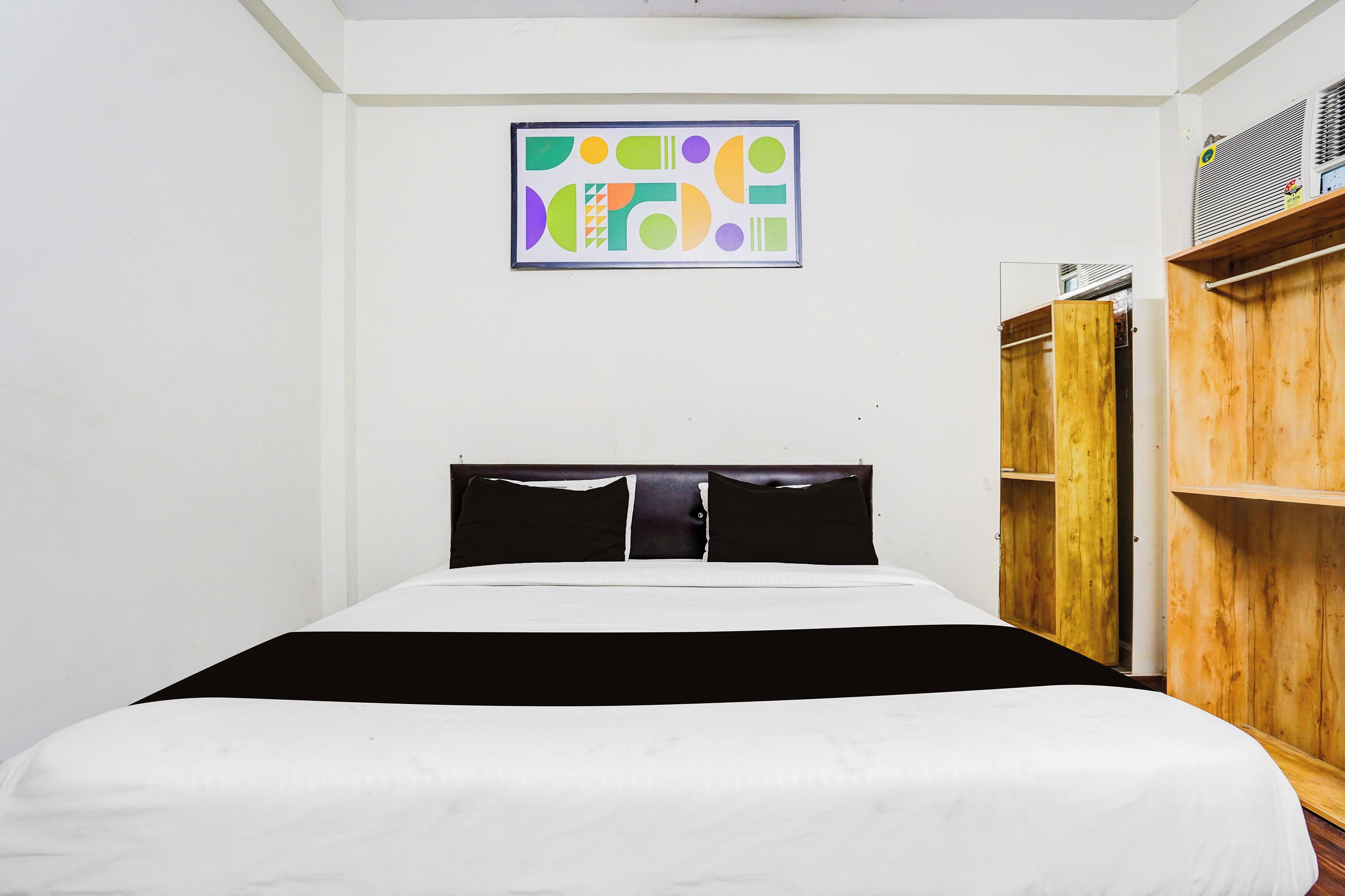 A bedroom with a bed, a wooden wardrobe, and a wall-mounted abstract art piece.