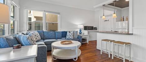 A modern living room with a sectional sofa, a round coffee table, and a kitchen area with a white countertop and bar stools.