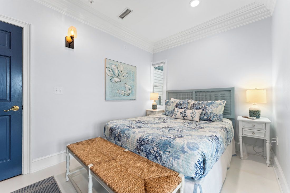 A bedroom with a bed, a bench, a nightstand, a lamp, and a door.