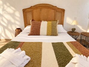 A neatly made bed with a striped area rug, a wooden headboard, and a bedside table with a lamp. - Bergerie Murtinella (Olmeto)