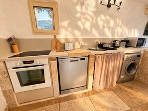 A compact kitchen with a built-in oven, dishwasher, and washing machine, a window with a view, and a small countertop with various appliances. - Bergerie Murtinella (Olmeto)