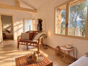 Quarto aconchegante com um sofá de vime, uma mesa de madeira pequena, parede de pedra e vista para o exterior.