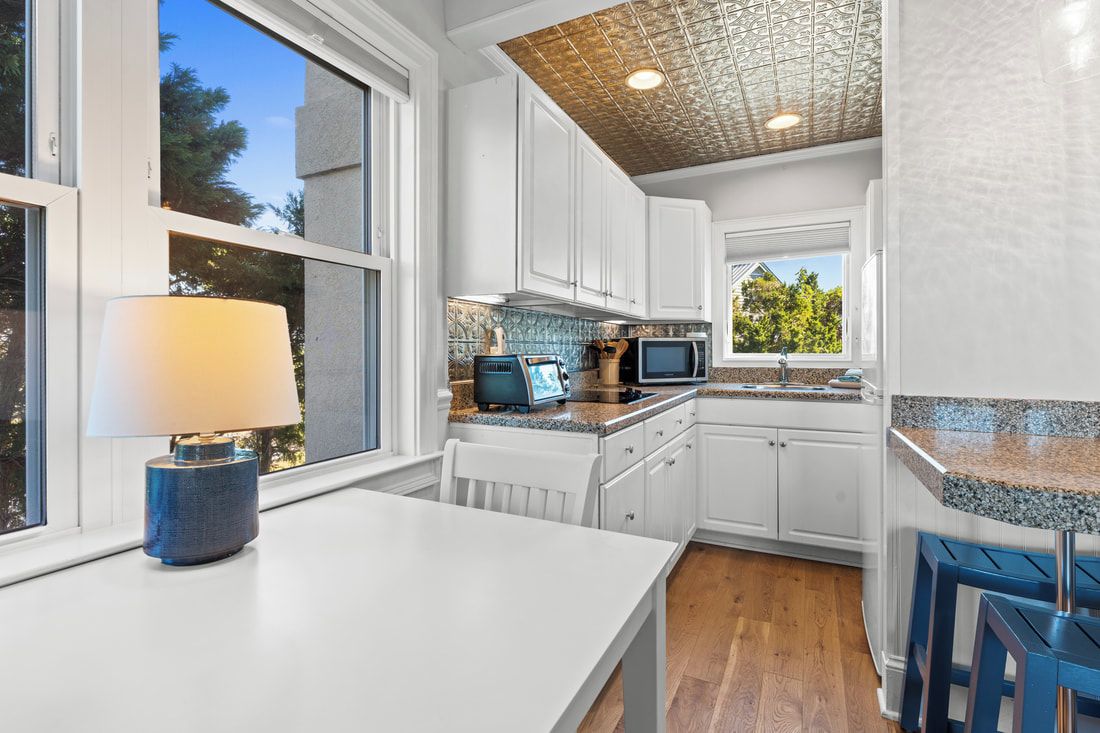 A kitchen with white cabinets, a granite countertop, a microwave, a toaster, and a window with a view of trees.