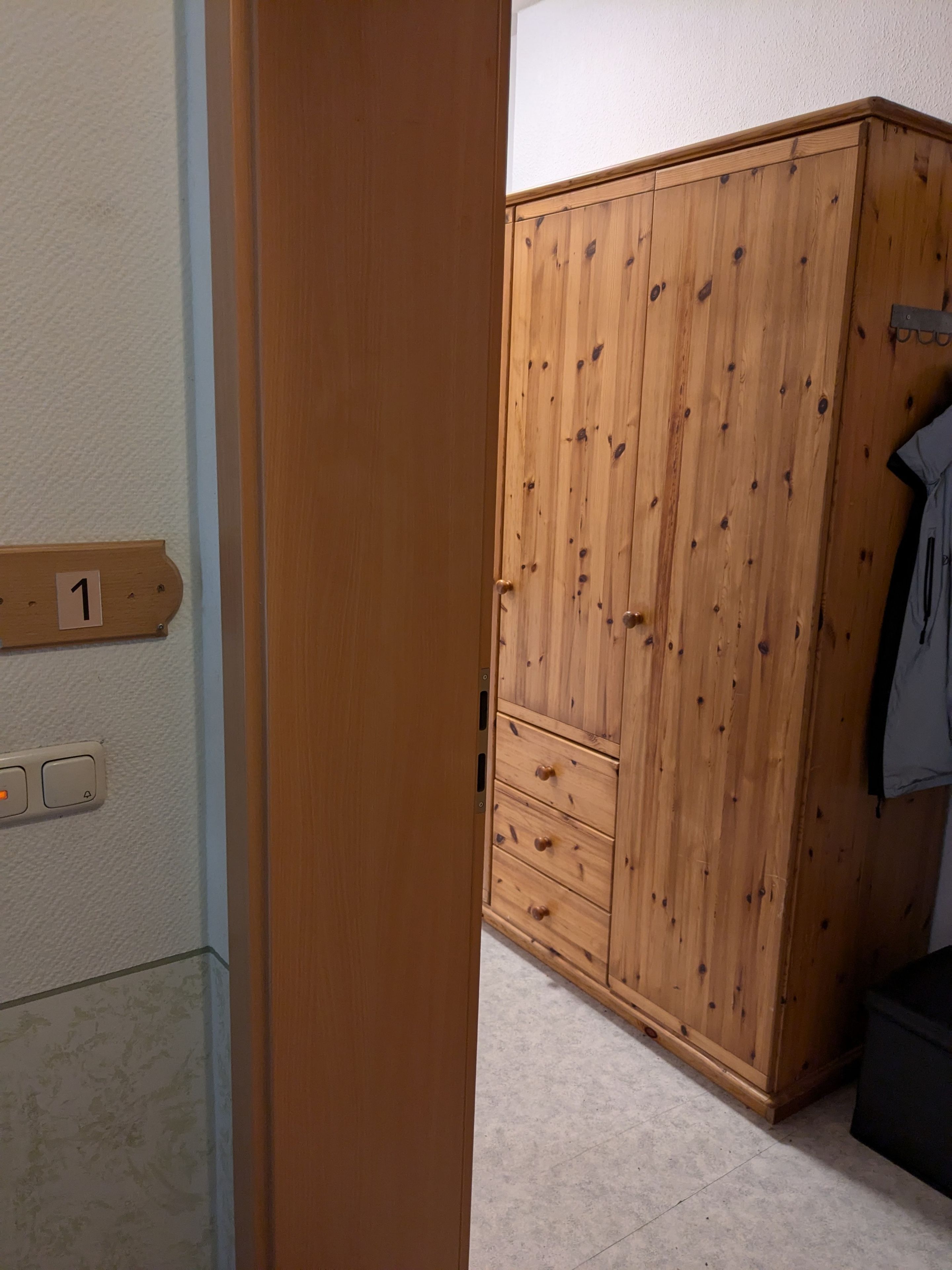 Et træskab med skuffer og en frakke hængende på højre side.