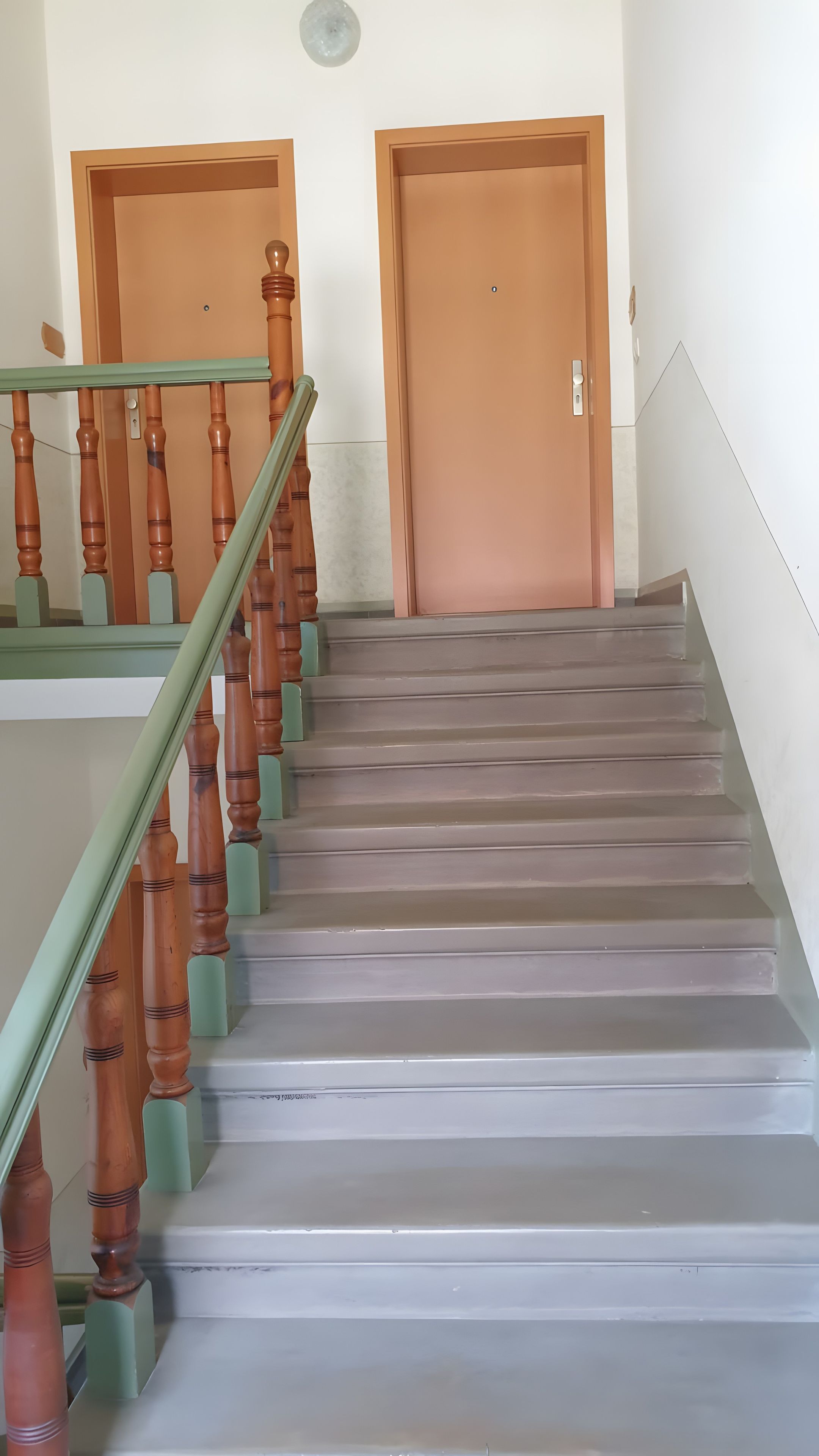 Een trap met houten spijbels en een groene leuning die uitkomt op een plateau met twee deuren.