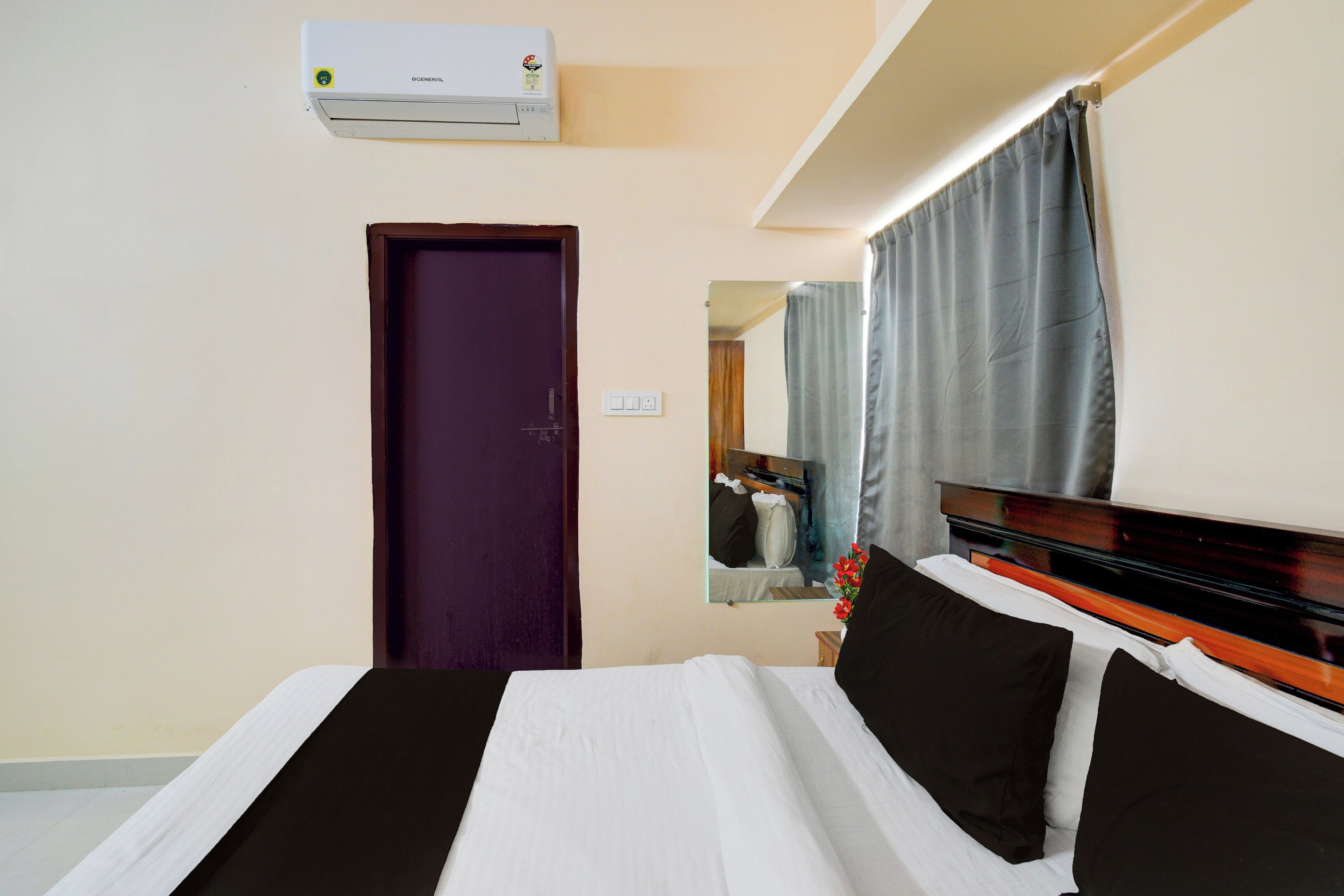 A hotel room with a bed, a door, a mirror, and an air conditioning unit.