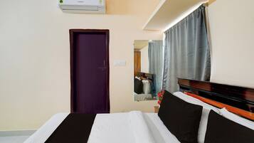 A hotel room with a bed, a door, a mirror, and an air conditioning unit.