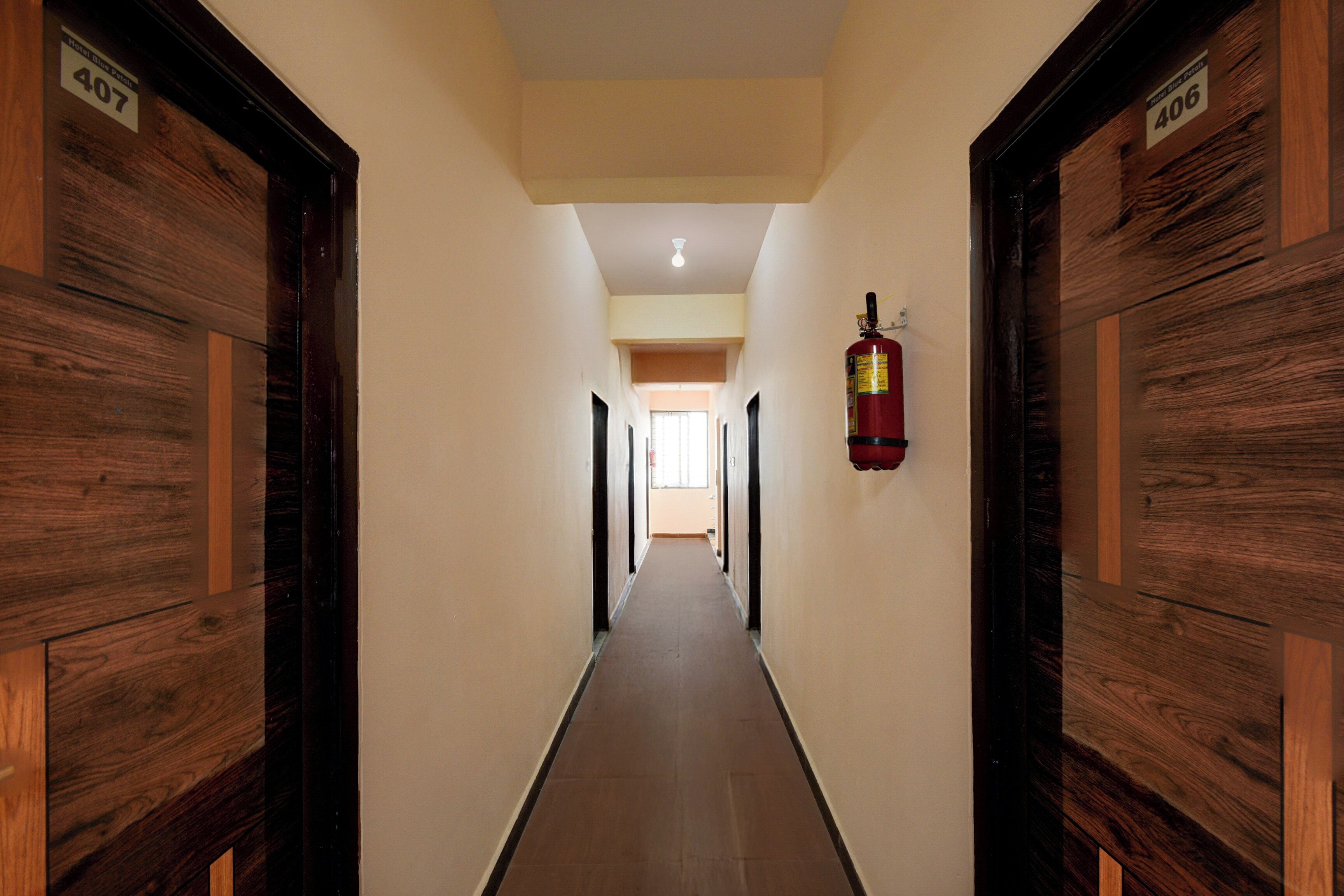 Un pasillo de hotel con puertas de madera identificadas como 407 y 406, un extintor de incendios en la pared y suelo de baldosas.
