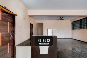Zona de recepción de un hotel con puerta de madera, un letrero que indica que es un hotel de servicios corporativos y un ventilador de techo.