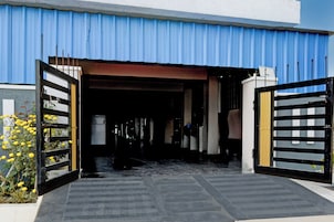 A building entrance with a blue corrugated roof, a gated driveway, and a pathway leading to the entrance.