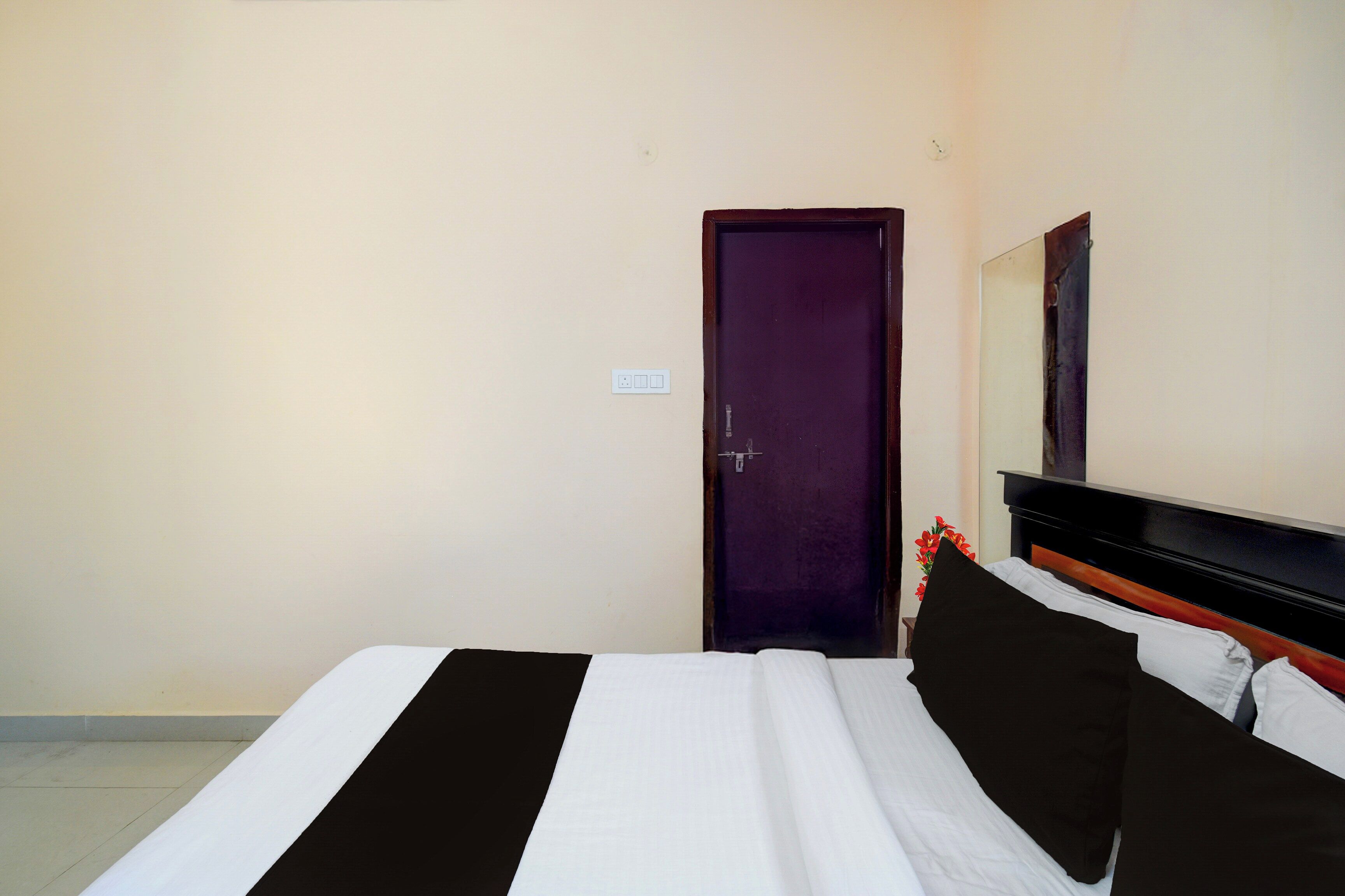 Habitació d'hotel amb un llit, una porta, un mirall fixat a la paret i una petita planta.