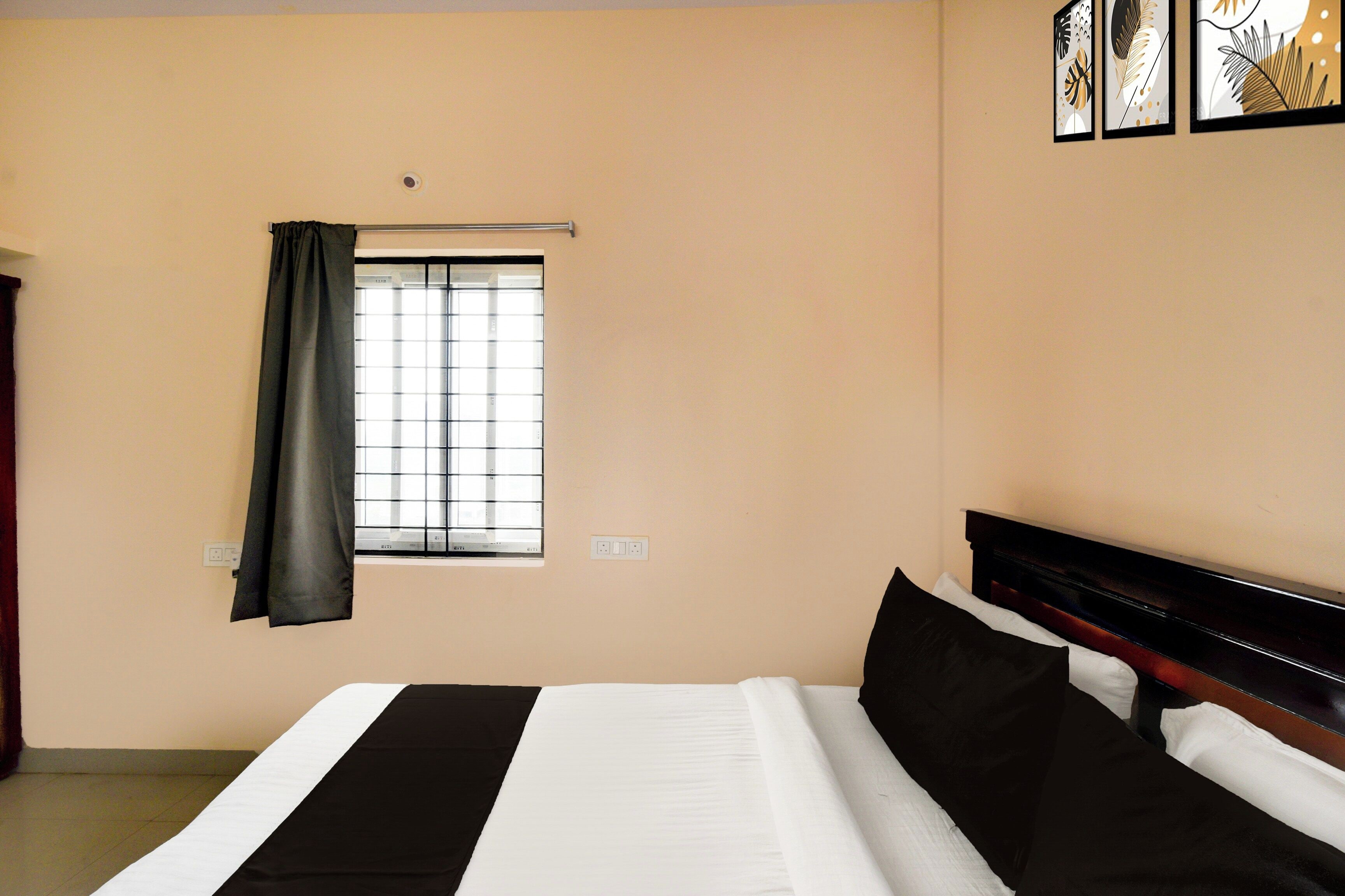 Habitación de hotel con cama, ventana con cortinas, interruptor de luz en la pared y un cuadro enmarcado.