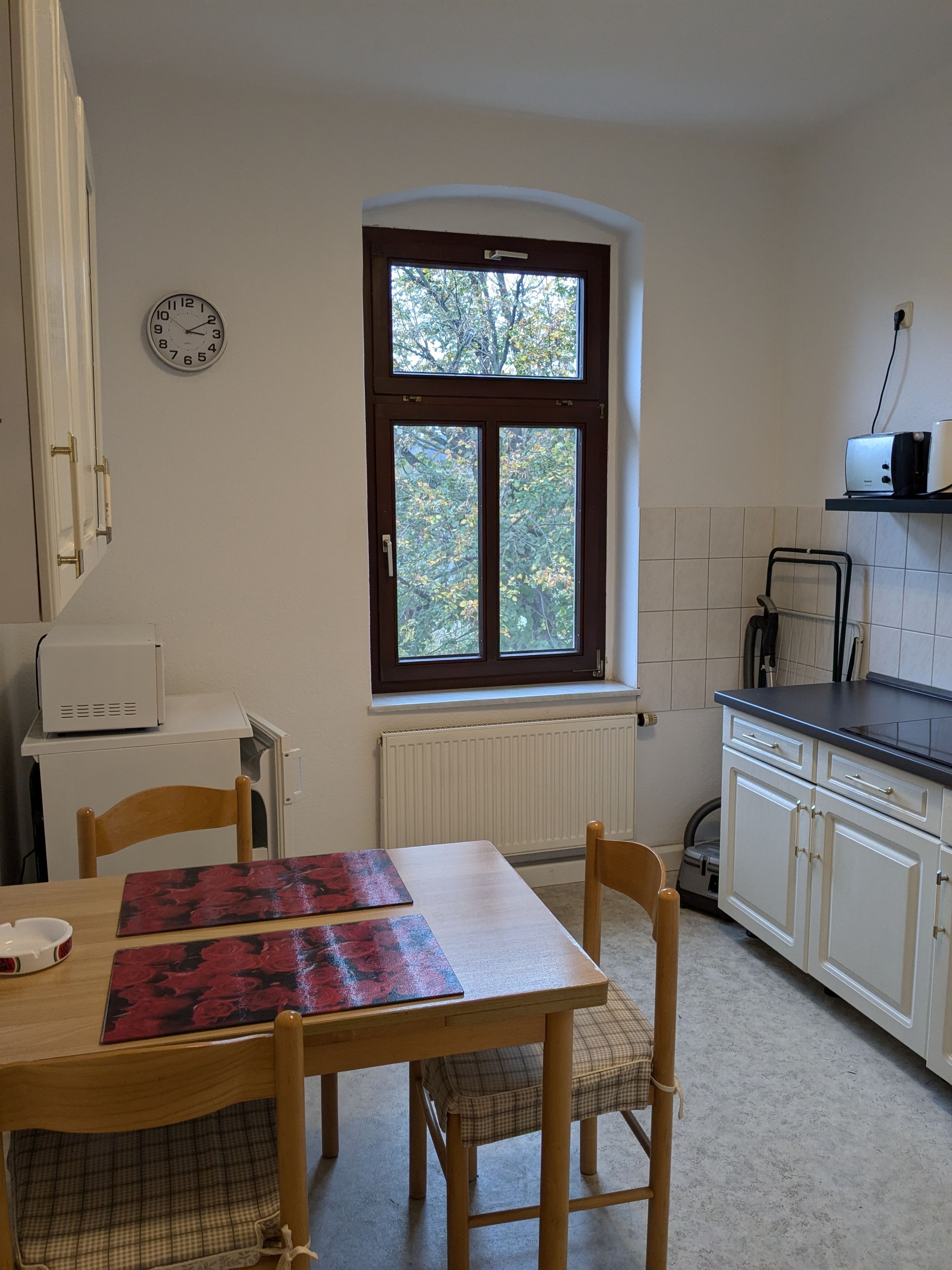 A kitchen with a window, a clock, a toaster, and a table with chairs.