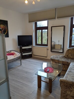 A living room with a television, sofa, and a glass coffee table. - Apartment 'Zuhause auf Zeit' with Garden (Gera)