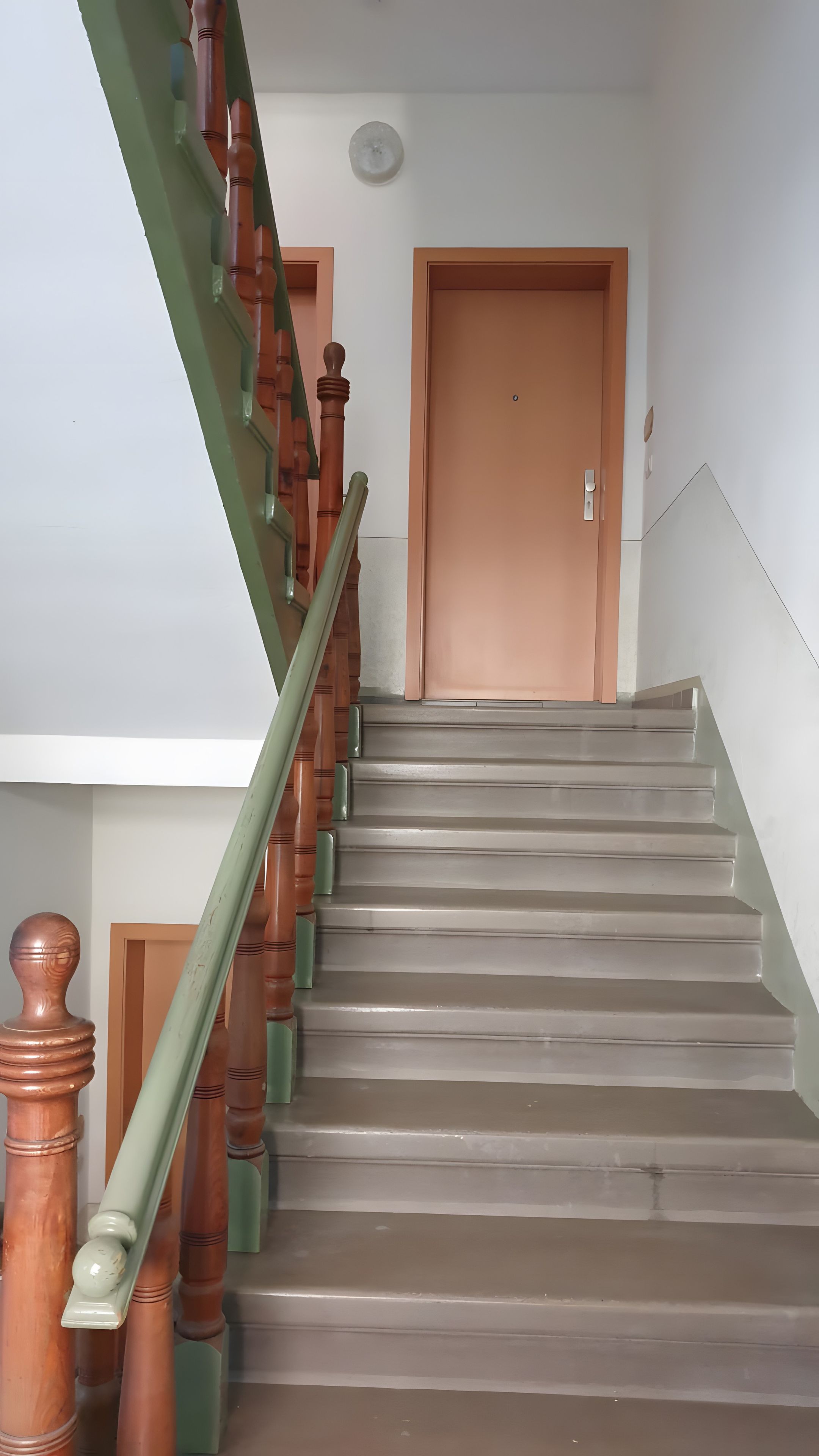 Eine Treppe mit Holzspindeln und einem grünen Geländer, das zu einer geschlossenen Tür führt.