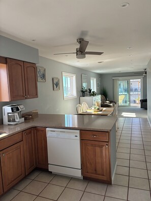 A kitchen with wooden cabinets, a dishwasher, a coffee maker, and a dining area with chairs and a table. - 2 bedroom/bath condo in Midtown--1.5 blocks from OCMD beach (Ocean City)