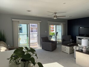 A living room with a ceiling fan, a television, and a sliding glass door leading to a balcony. - 2 bedroom/bath condo in Midtown--1.5 blocks from OCMD beach (Ocean City)