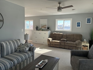 Ein Wohnzimmer mit einem gestreiften Sofa, einem gepolsterten Sofa, einem Couchtisch, einer weißen Kommode und einem Deckenventilator.
