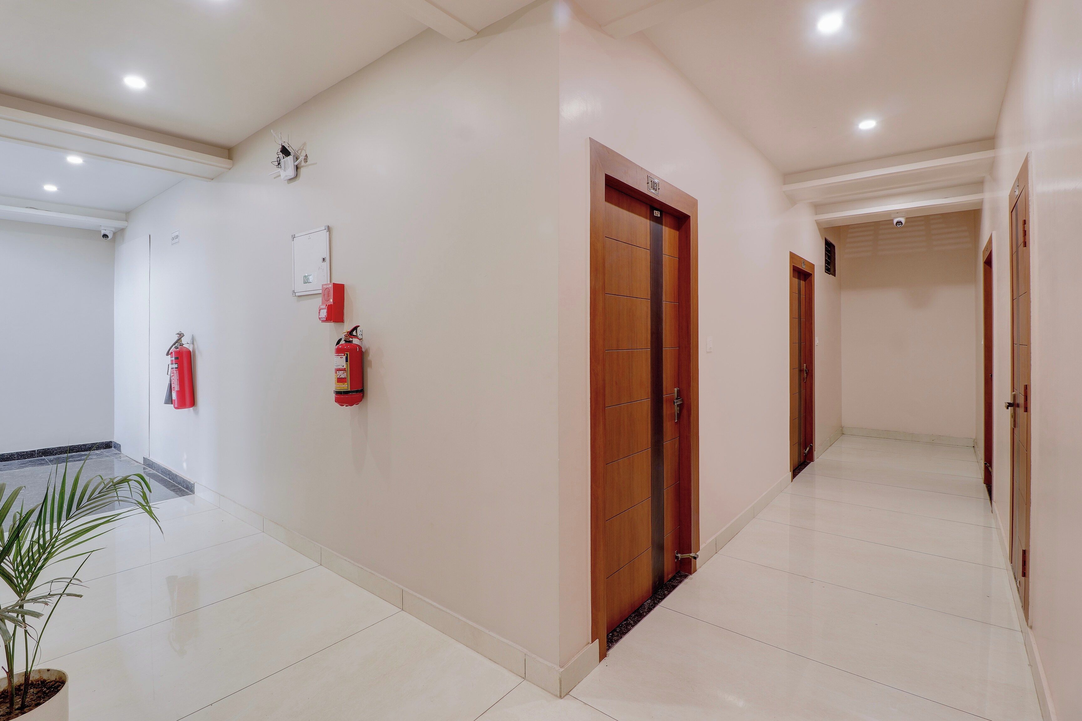 Corredor limpo e bem iluminado, com extintor de incêndio, alarme de incêndio e uma porta que dá para outro cômodo.