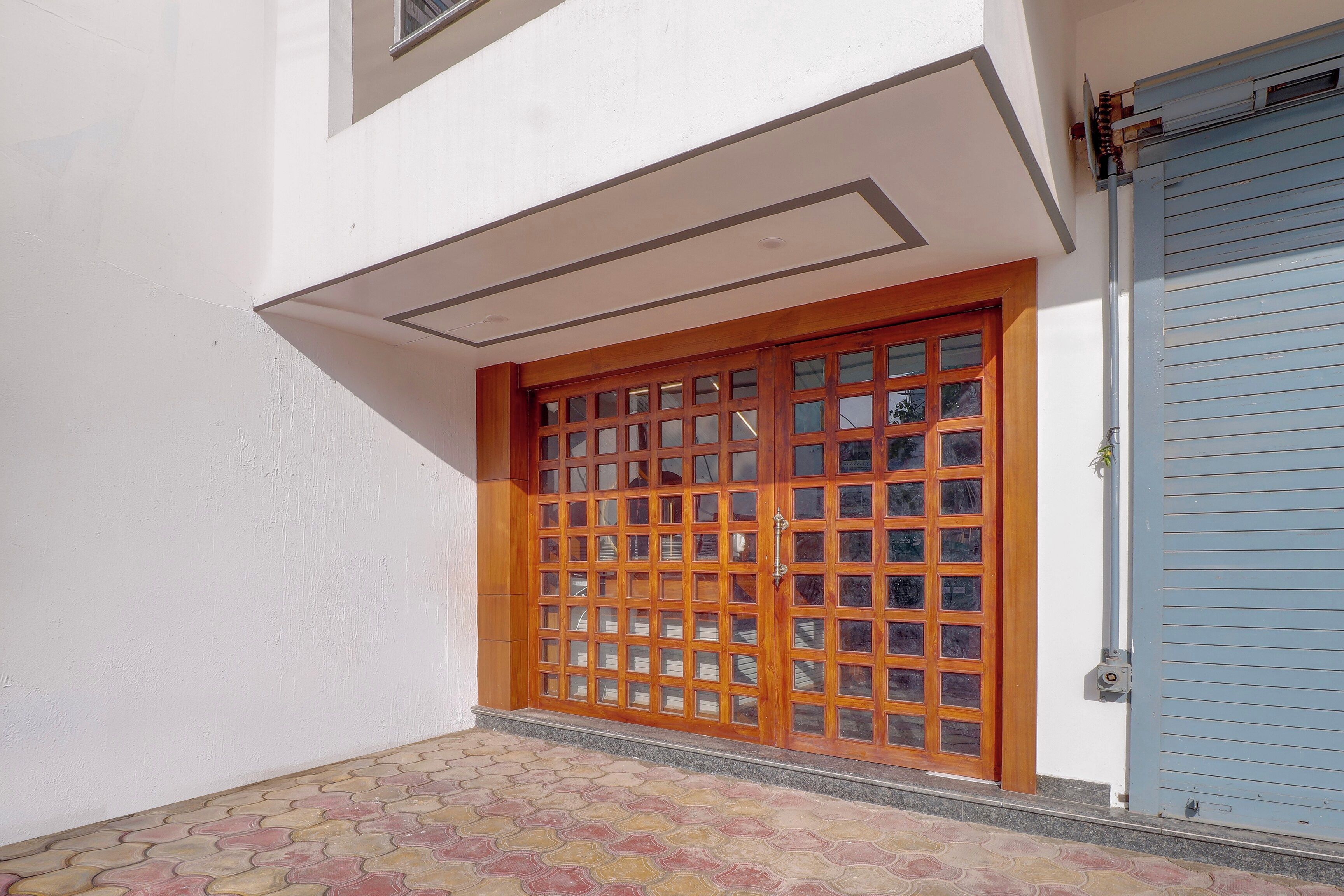 Una entrada de edificio con un portón de madera, una puerta azul y un pavimento adoquinado.