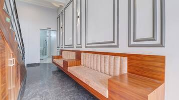 Un área de recepción moderna con un banco de madera, un vidrio que da a una oficina y un piso de mármol pulido.