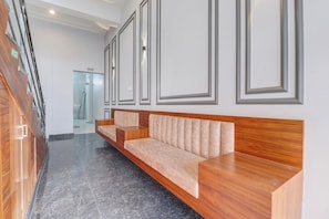 Un área de recepción moderna con un banco de madera, un vidrio que da a una oficina y un piso de mármol pulido.