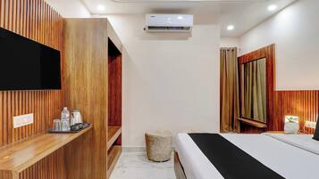 Una habitación de hotel moderna con una cama, televisión, pared de paneles de madera, una pequeña zona de estar y un aire acondicionado instalado en el techo.