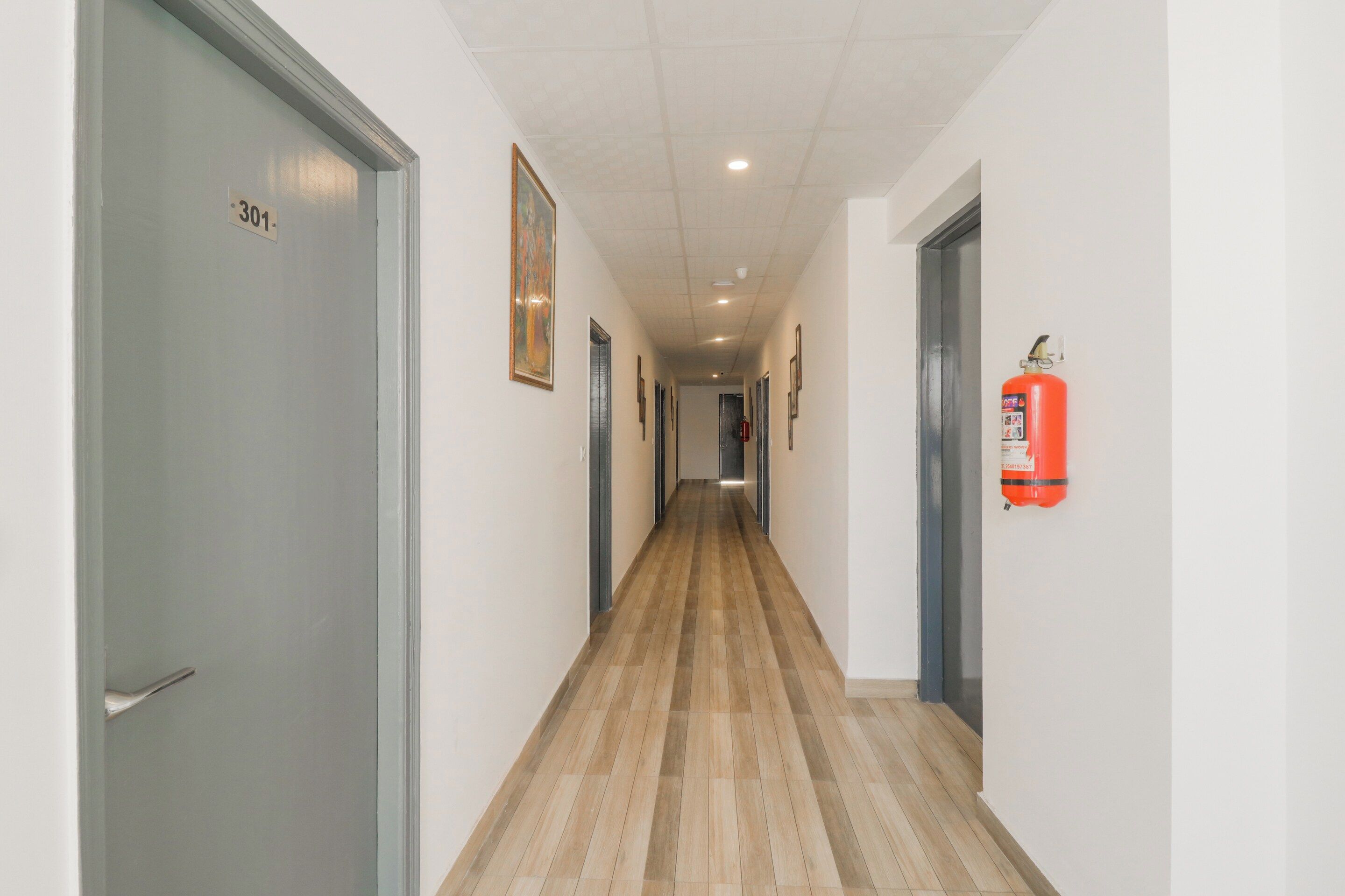 A corridor with doors on both sides, a fire extinguisher mounted on the wall, and a ceiling with recessed lighting.