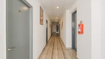 A corridor with doors on both sides, a fire extinguisher mounted on the wall, and a ceiling with recessed lighting.