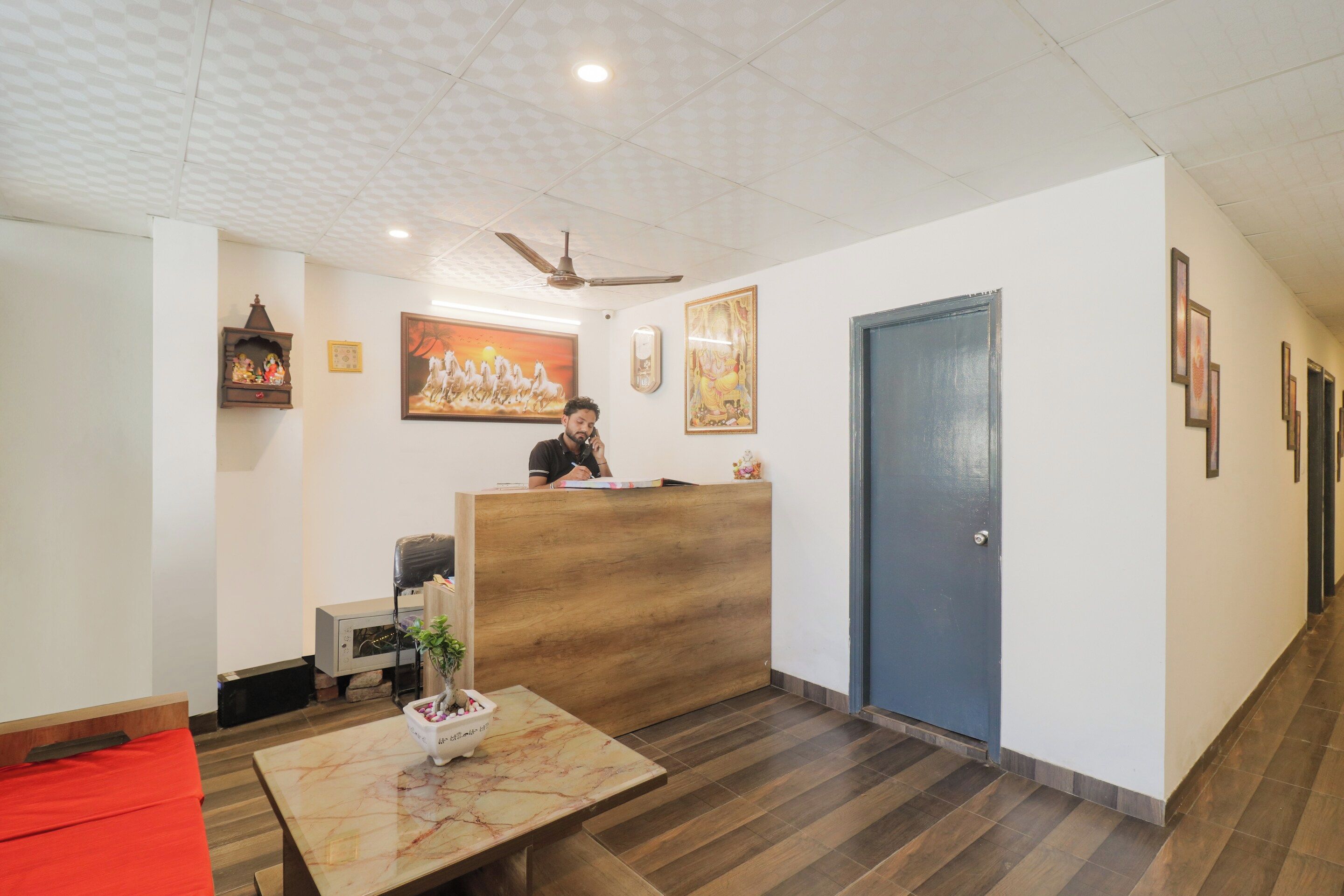 A reception area with a wooden desk, a seated receptionist, a wall-mounted clock, and framed artwork.