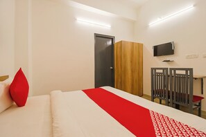 Una habitación de hotel con una cama, un armario de madera, un escritorio con una silla y un televisor montado en la pared.