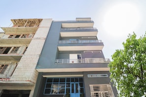 A multi-story building with balconies, a blue door, and a construction site on the left. - Hotel O Perky Stay (Faridabad)