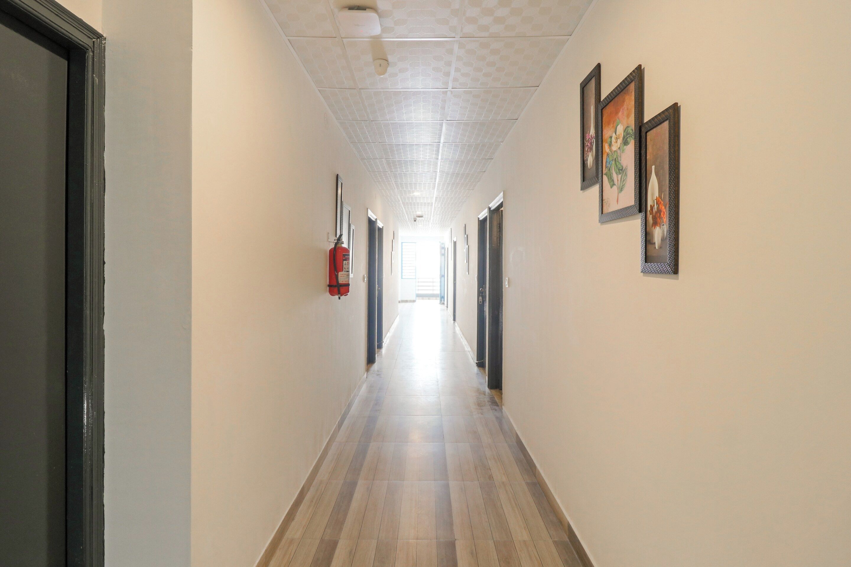 A long, narrow hallway with a fire extinguisher mounted on the wall, a ceiling with a grid pattern, and framed artwork on the walls.