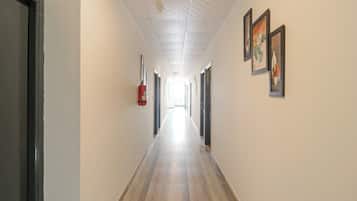 A long, narrow hallway with a fire extinguisher mounted on the wall, a ceiling with a grid pattern, and framed artwork on the walls.