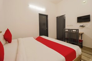 Habitación de hotel con cama, televisor montado en la pared y escritorio con silla.