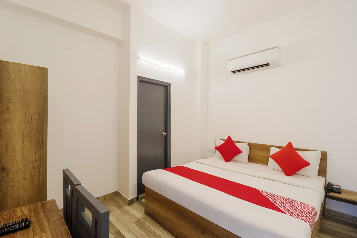 A hotel room with a bed, a desk, a chair, an air conditioning unit, and a door.