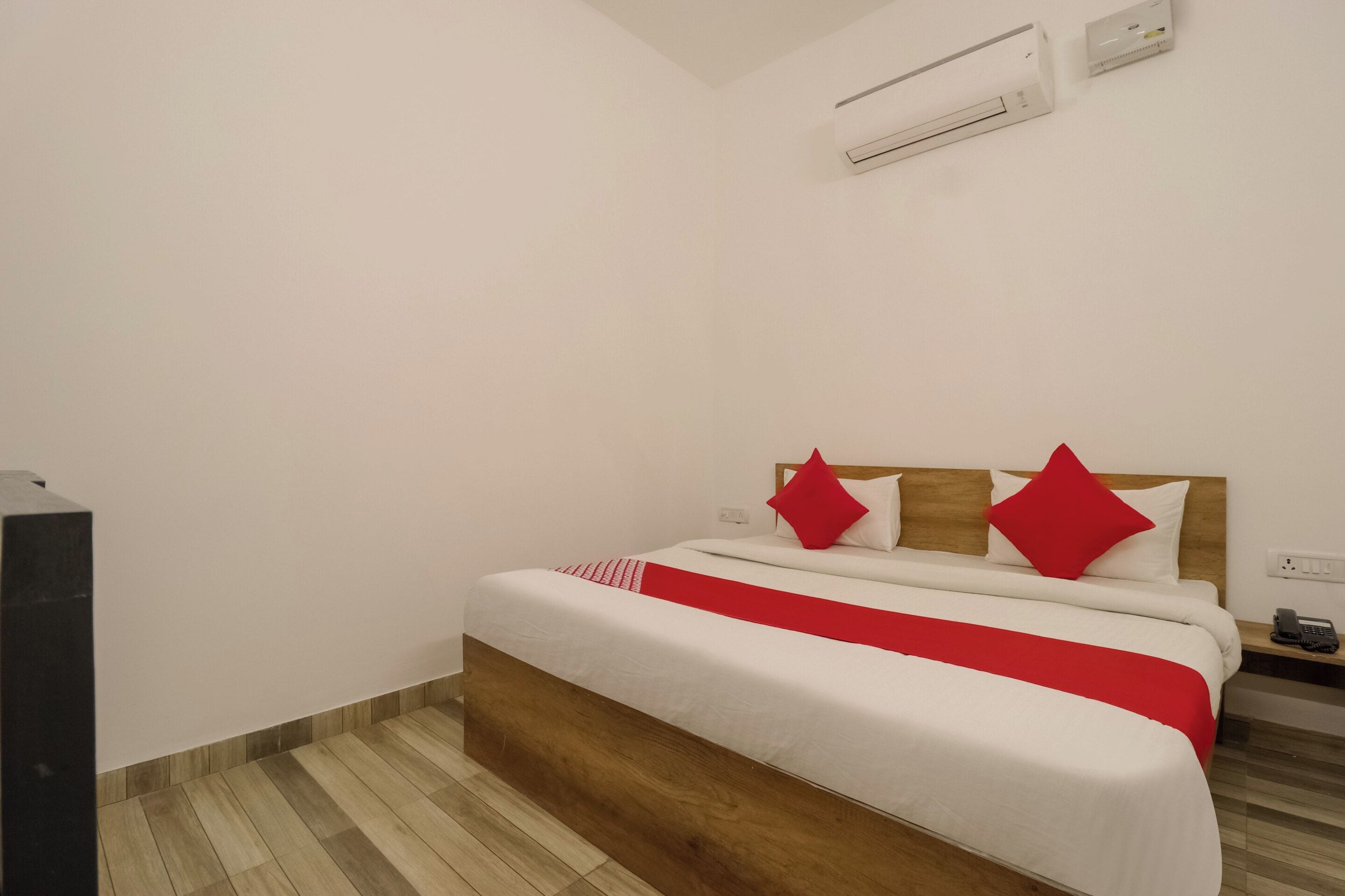 A bedroom with a bed, a wooden headboard, a red and white bedspread, and a white wall.