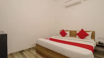 A bedroom with a bed, a wooden headboard, a red and white bedspread, and a white wall.