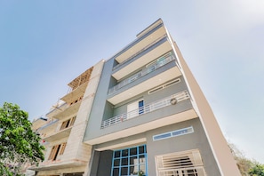 A multi-story building with balconies and a window with a blue frame. - Hotel O Perky Stay (Faridabad)