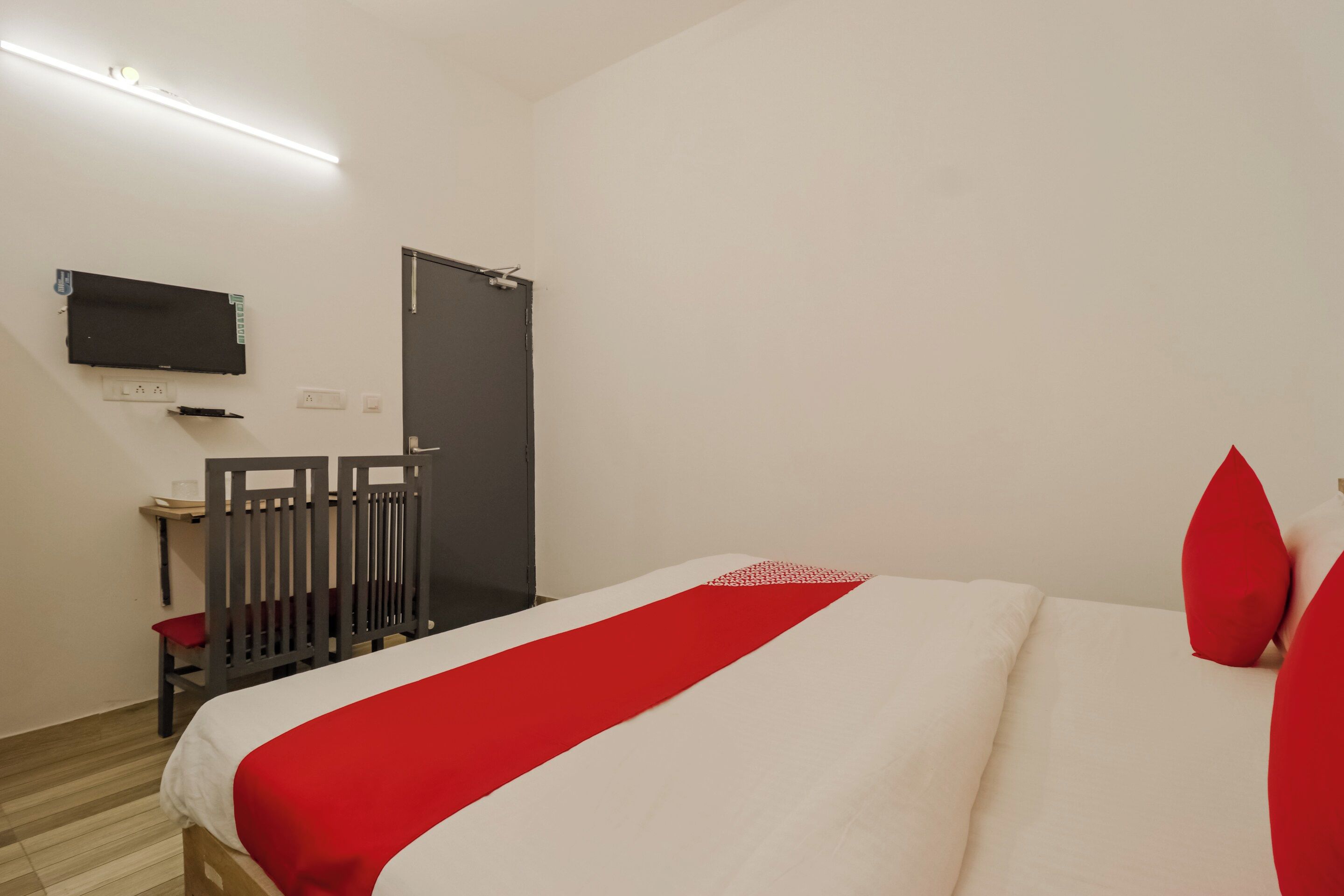A hotel room with a bed, a TV mounted on the wall, a door, and a small table with a chair.