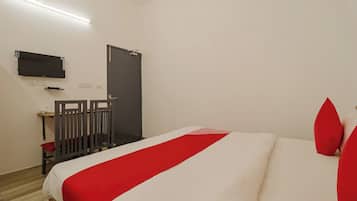A hotel room with a bed, a TV mounted on the wall, a door, and a small table with a chair.