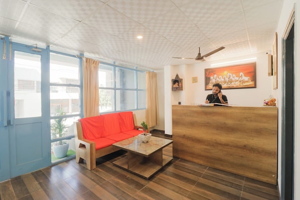 A reception area with a wooden reception desk, a red sofa, a coffee table, and a ceiling fan. - Hotel O Perky Stay (Faridabad)