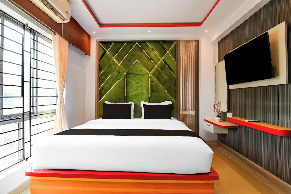 A hotel room with a bed, a TV mounted on the wall, and a window with blinds.